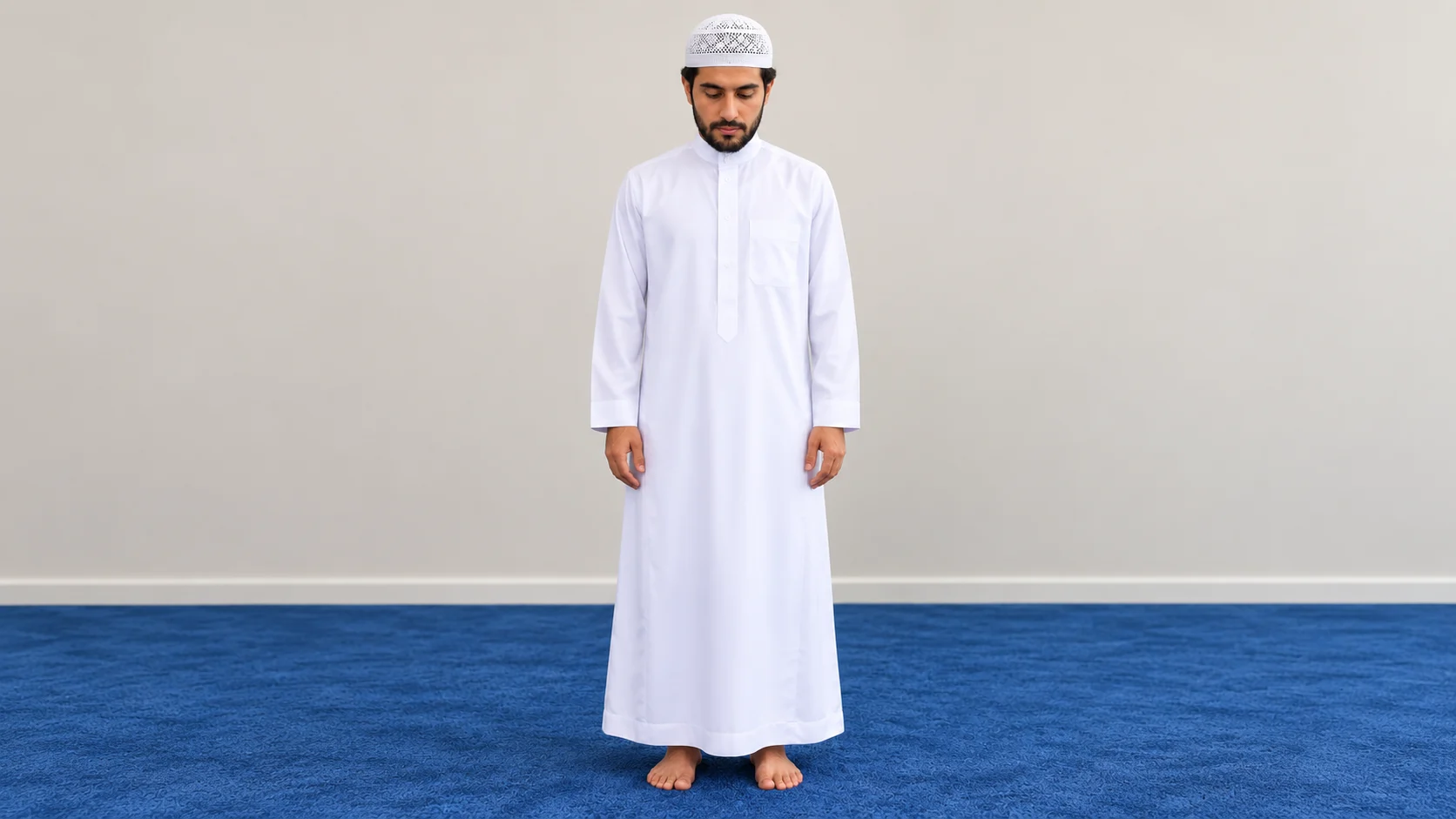 Le même homme en qamis blanc et kufi blanc que dans la photographie de référence, debout calmement sur le tapis bleu, les mains relâchées et le regard baissé.