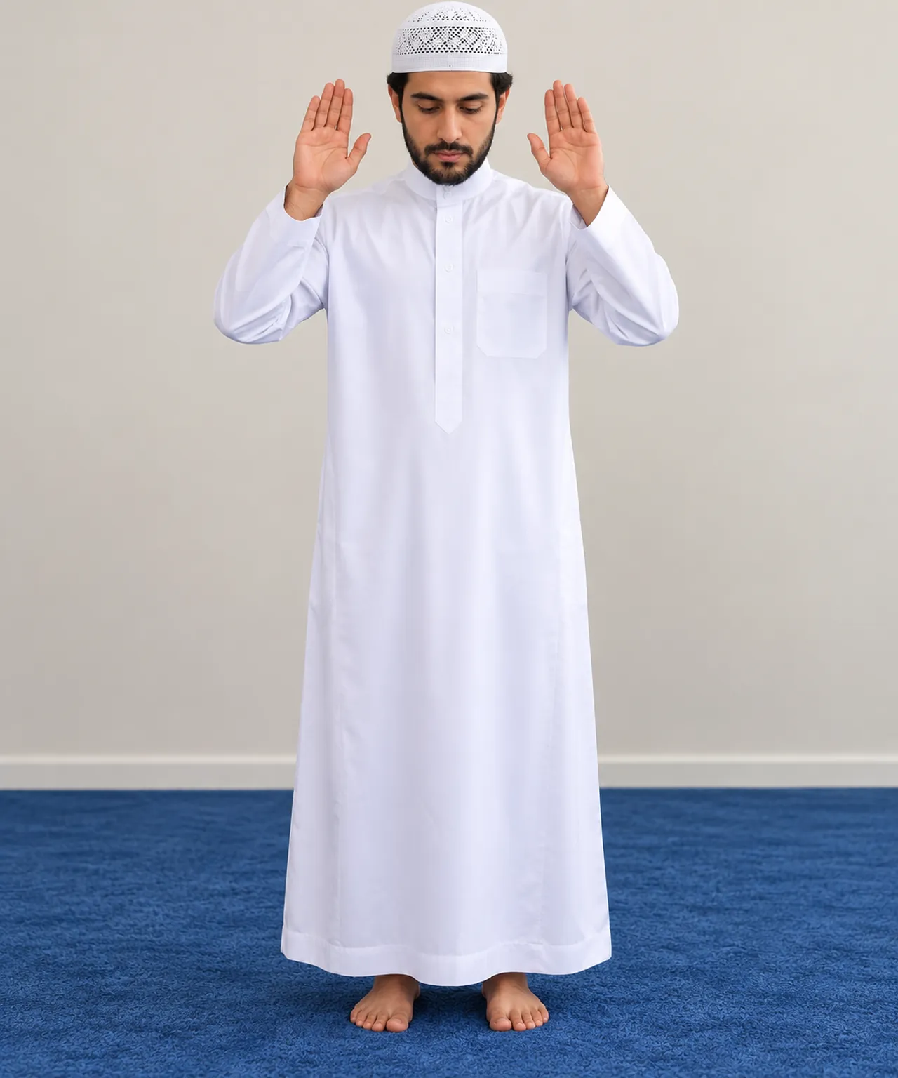 Homme debout sur un tapis de prière, mains levées à hauteur des épaules, paumes vers l’avant, pour le takbîr d’ouverture.